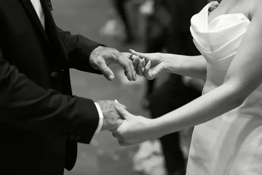 A close-up black and white shot captures the bride placing a wedding ring onto the groom's hand during the ceremony.