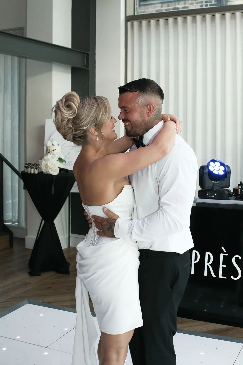 A bride and groom share a tender embrace during their first dance, with the bride wearing an elegant strapless white gown and a high bun.