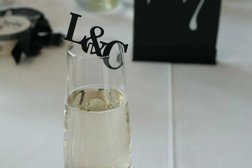 A close-up shot of a champagne flute adorned with a monogram drink marker on a white table linen setting.