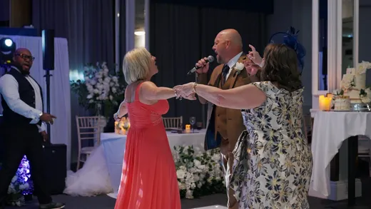 Guests enjoy lively dancing and singing during the evening wedding reception, with a singer holding a microphone while guests join hands on the dance floor.