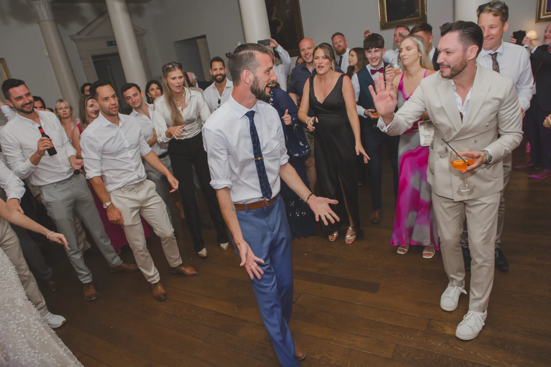 A lively group of wedding guests enjoying themselves on the dance floor in a grand manor house ballroom.