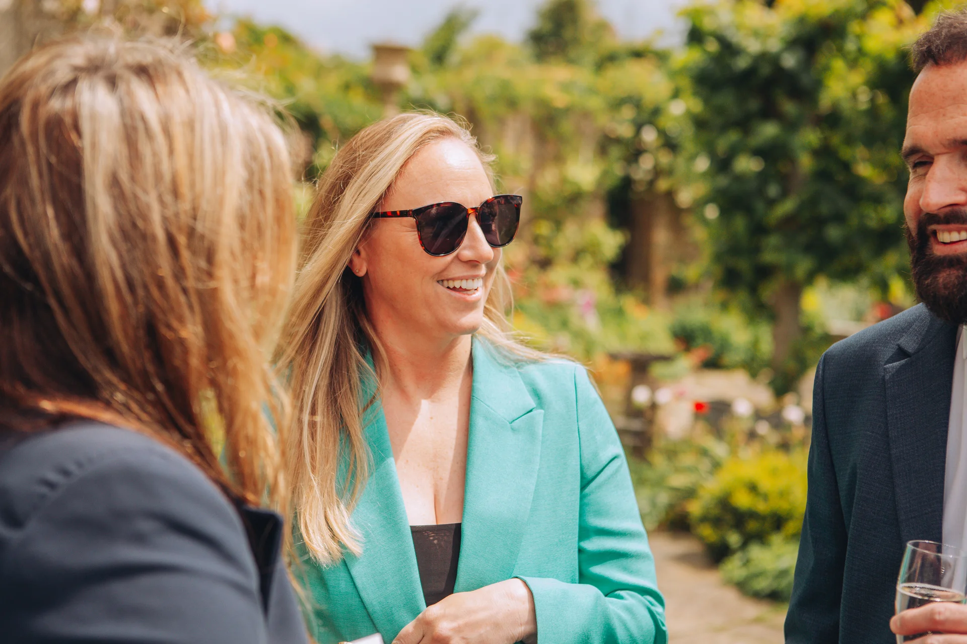 Wedding guests smiling and chatting outdoors in a sunny garden during the drinks reception.