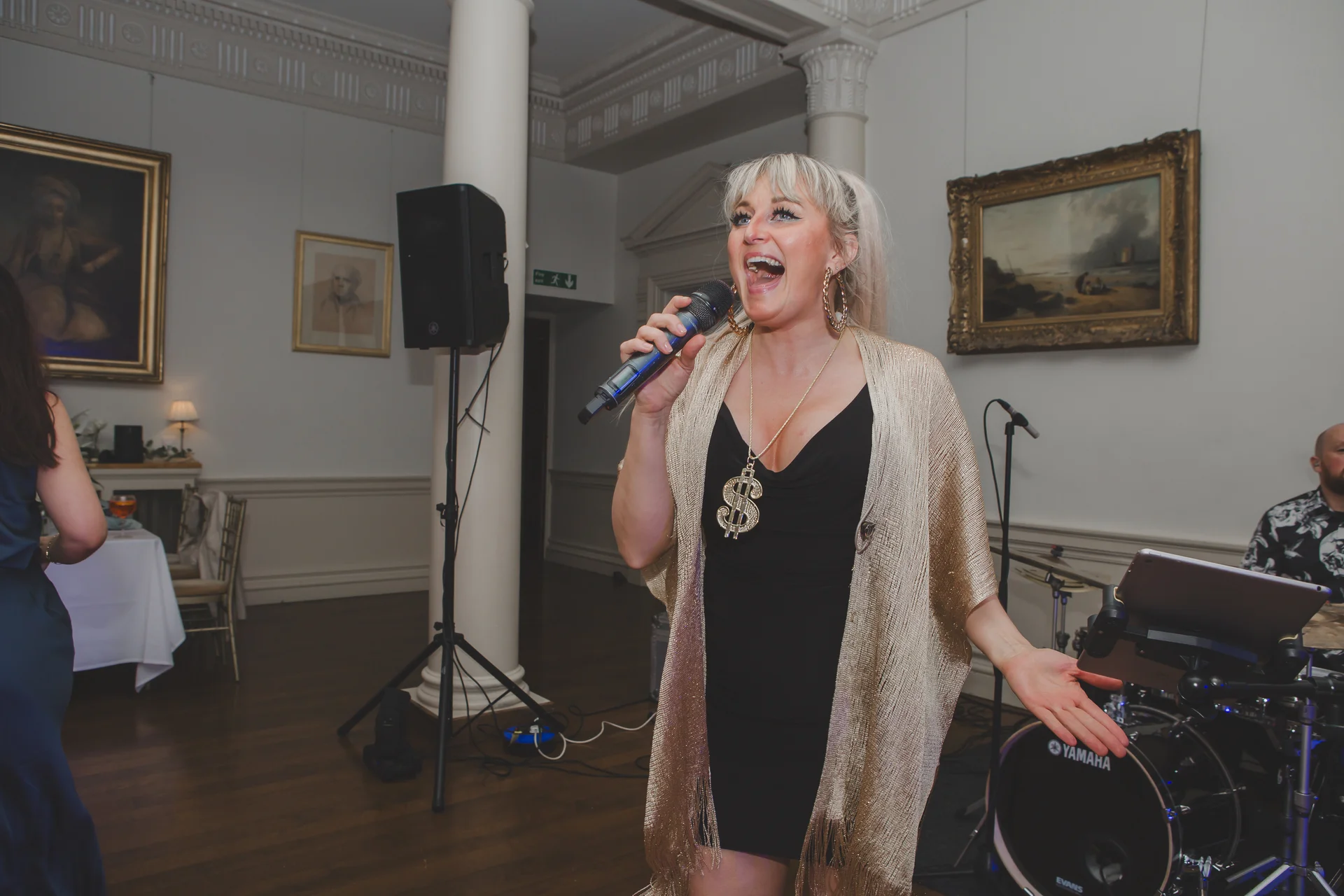 A female vocalist passionately sings into a microphone during a wedding reception in a stately venue.