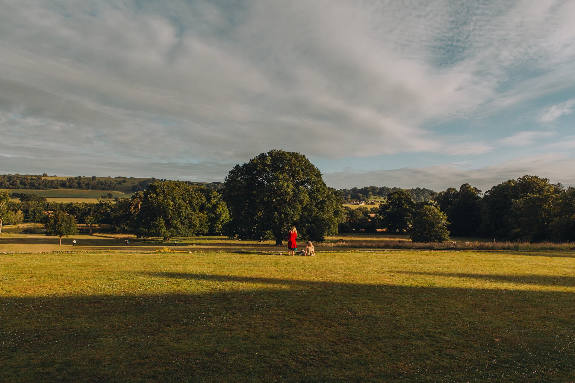 A tiny couple taking in the vast scenic landscape of a sprawling private estate under a dramatic cloudy sky.