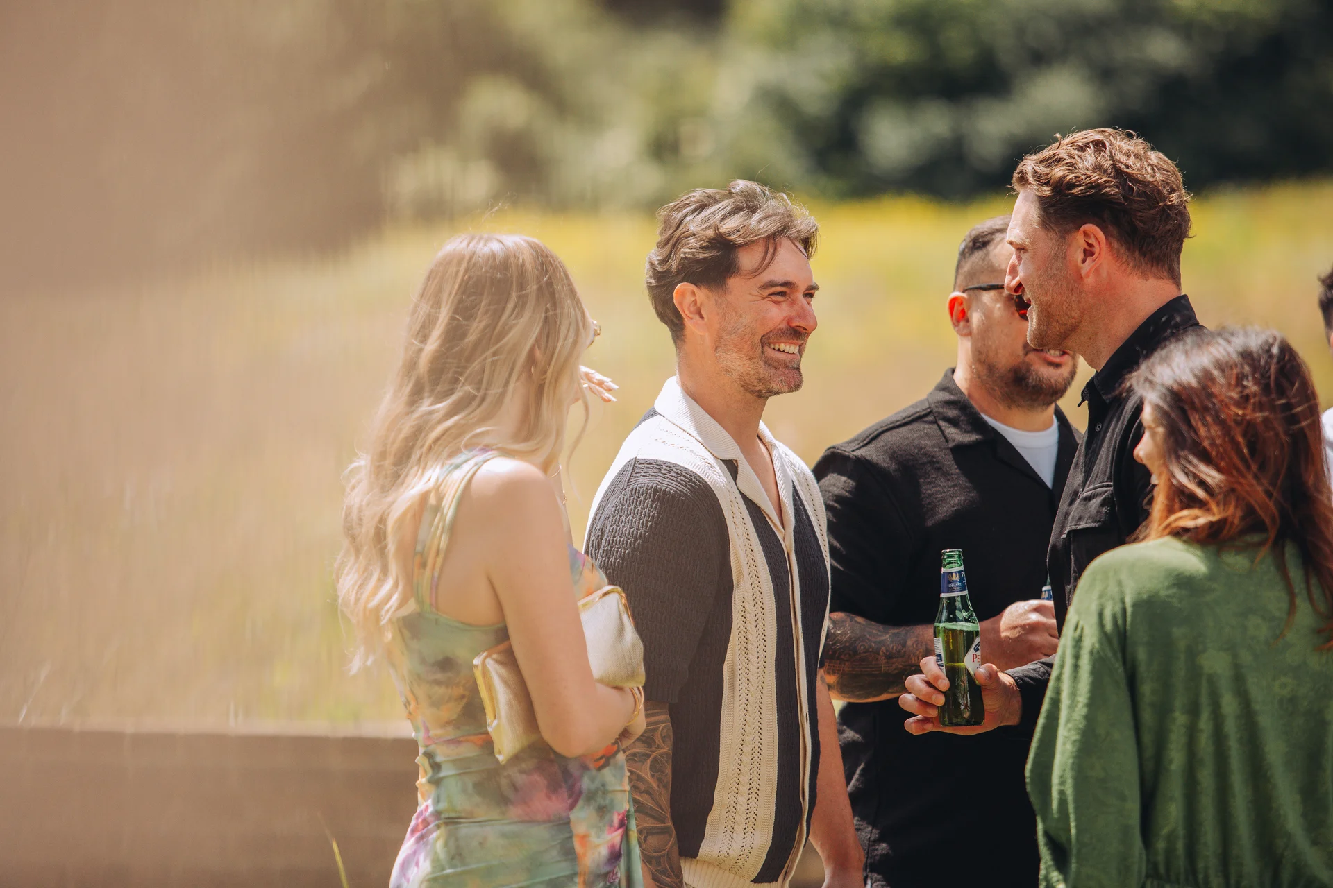 Wedding guests mingle and chat outdoors in the warm sunshine during a relaxed drinks reception.