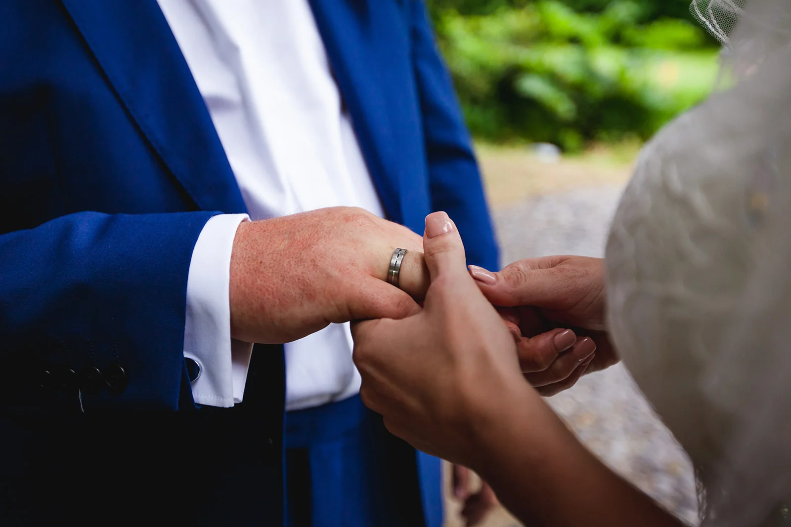 Close-up of a bride placing a wedding ring on the groom's finger during an outdoor ceremony.
