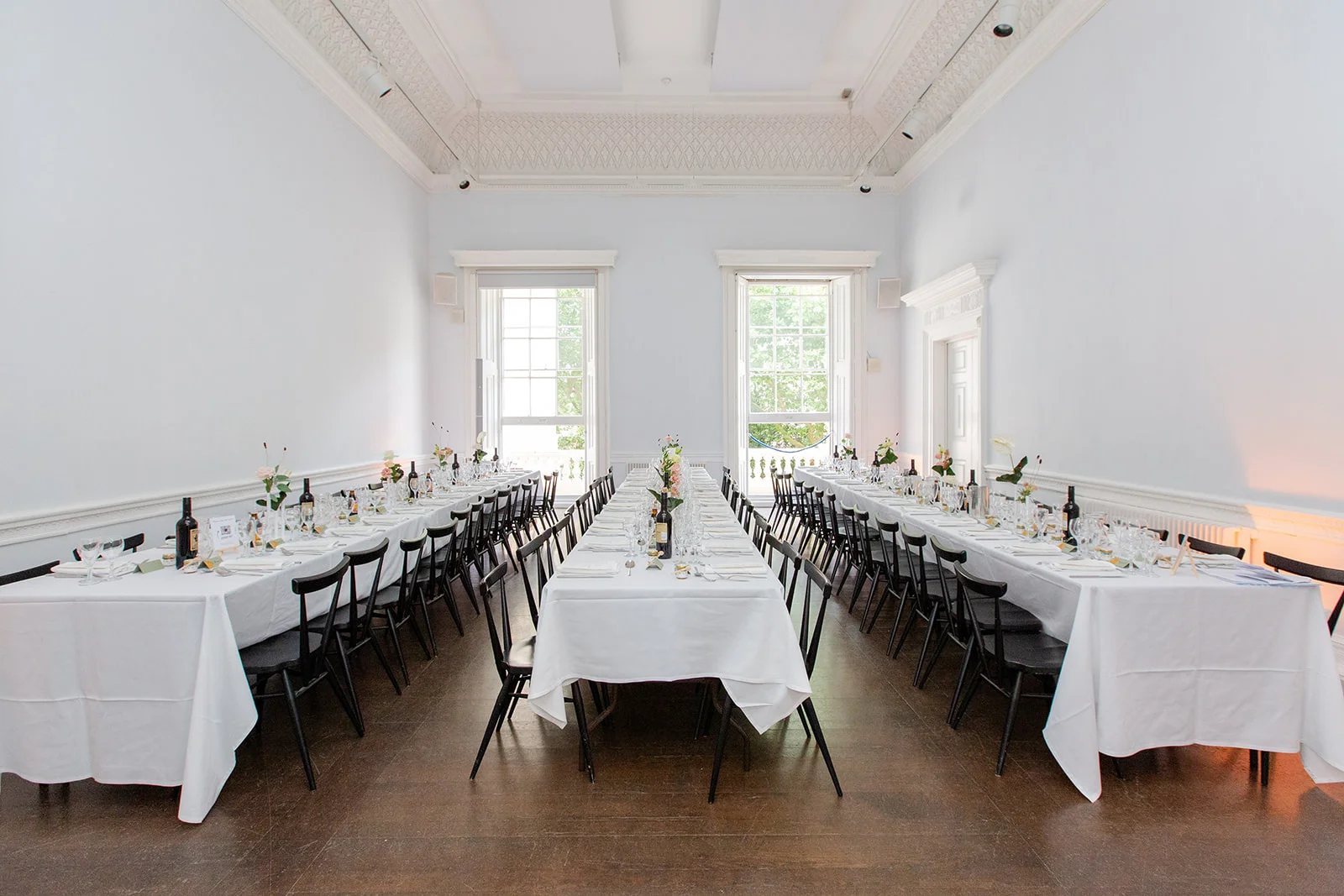 An elegant wedding breakfast reception setup in a bright, high-ceilinged hall featuring long banquet tables draped in white linens.