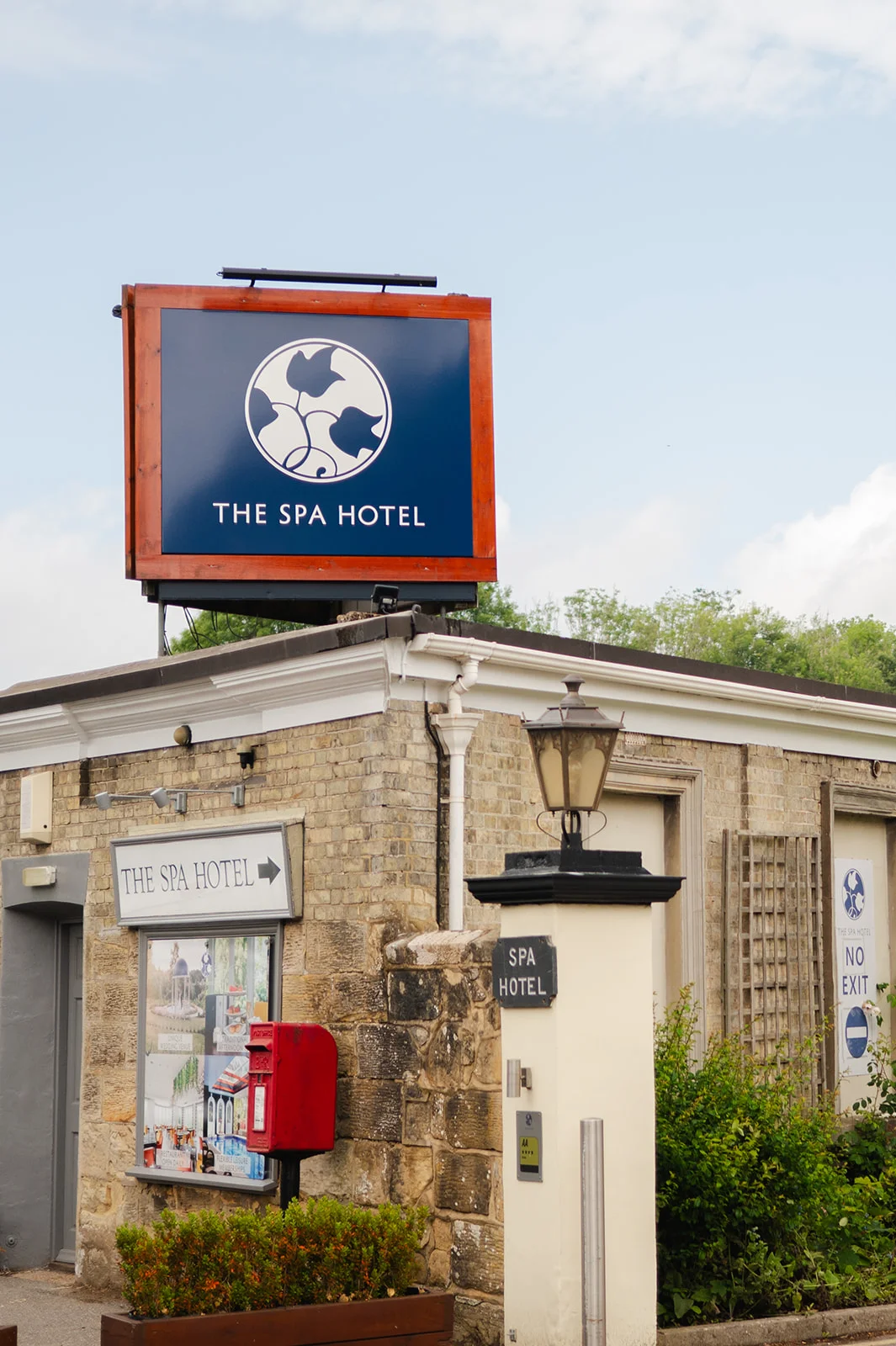 An exterior daytime shot of The Spa Hotel entrance sign mounted above a traditional brick building with a blue sky background.