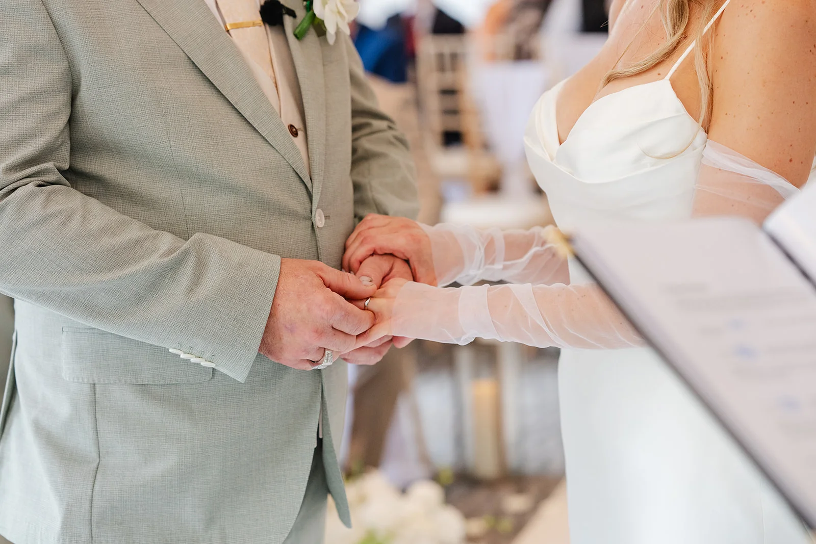 Close-up of a bride and groom holding hands and exchanging rings during their wedding ceremony.