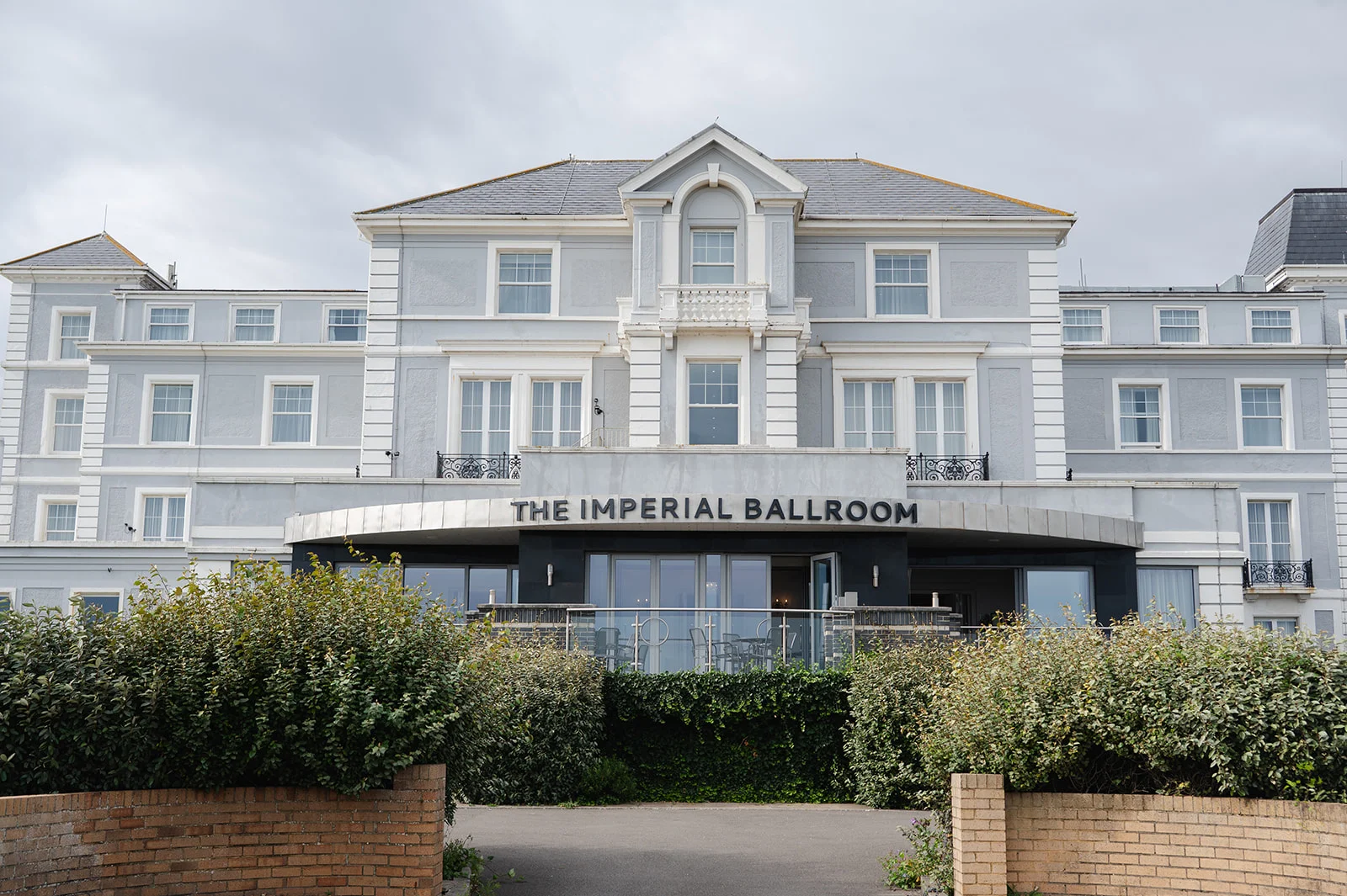 An exterior view of a grand grey hotel building featuring a prominent entrance sign reading The Imperial Ballroom under an overcast sky.