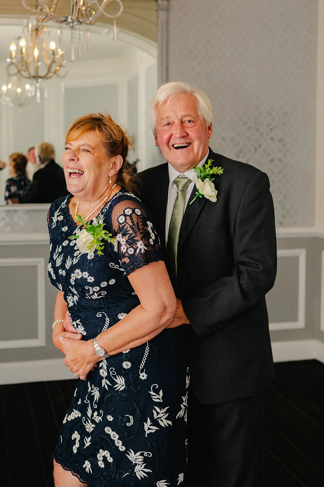 An older couple lovingly embraces and shares a joyful laugh indoors at a hotel wedding reception.