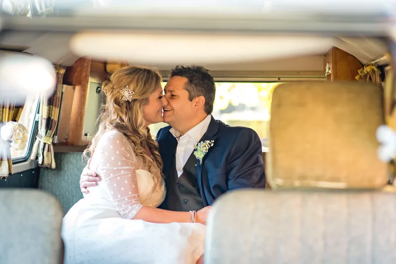 A newlywed couple share a tender kiss inside the vintage interior of a classic wedding campervan.