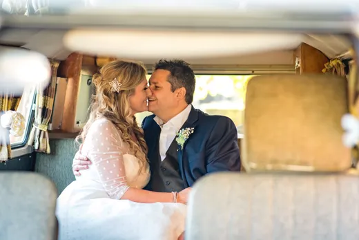 A newlywed couple share a tender kiss inside the vintage interior of a classic wedding campervan.