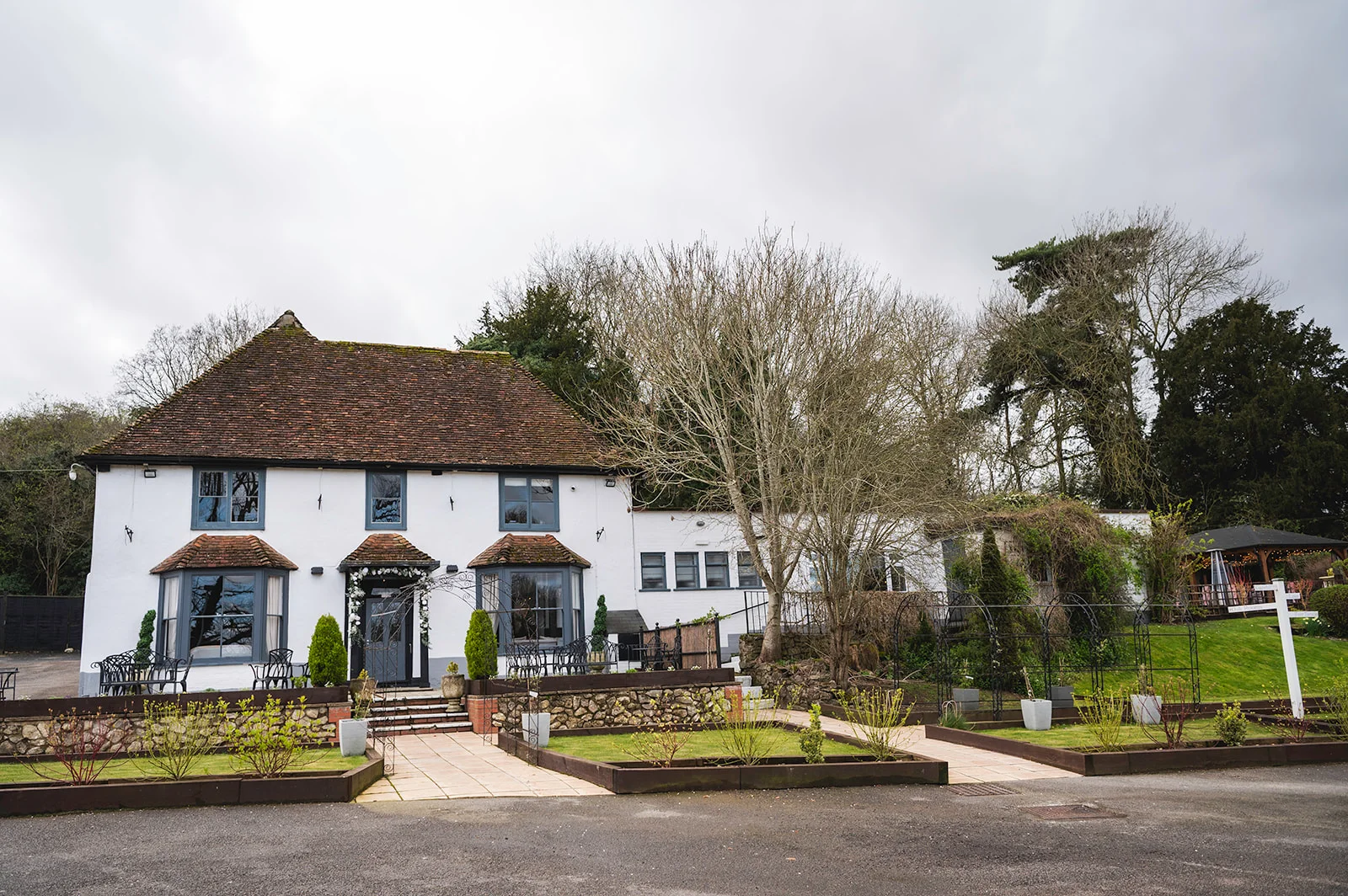 An exterior view of a charming white country house wedding venue with dark framed windows and manicured gardens under an overcast sky.