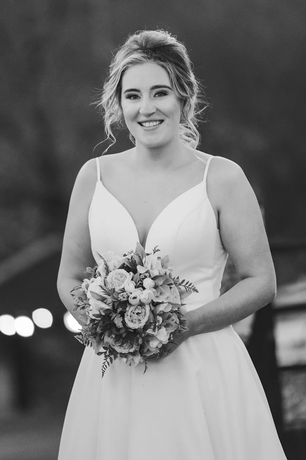A smiling bride wearing a v-neck a-line gown and holding a bouquet in a black and white portrait.