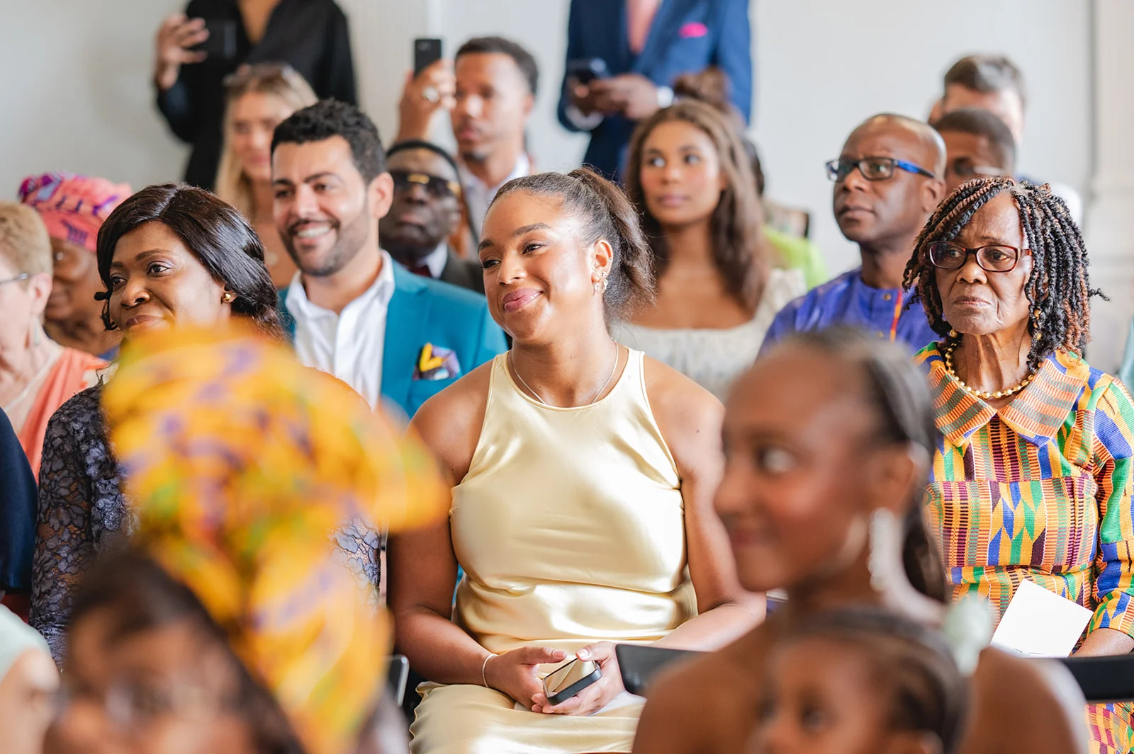 A diverse crowd of wedding guests smiling and watching the ceremony unfold indoors.