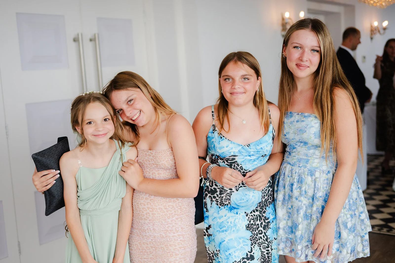 Four young wedding guests in colourful dresses smiling together indoors during the celebrations.