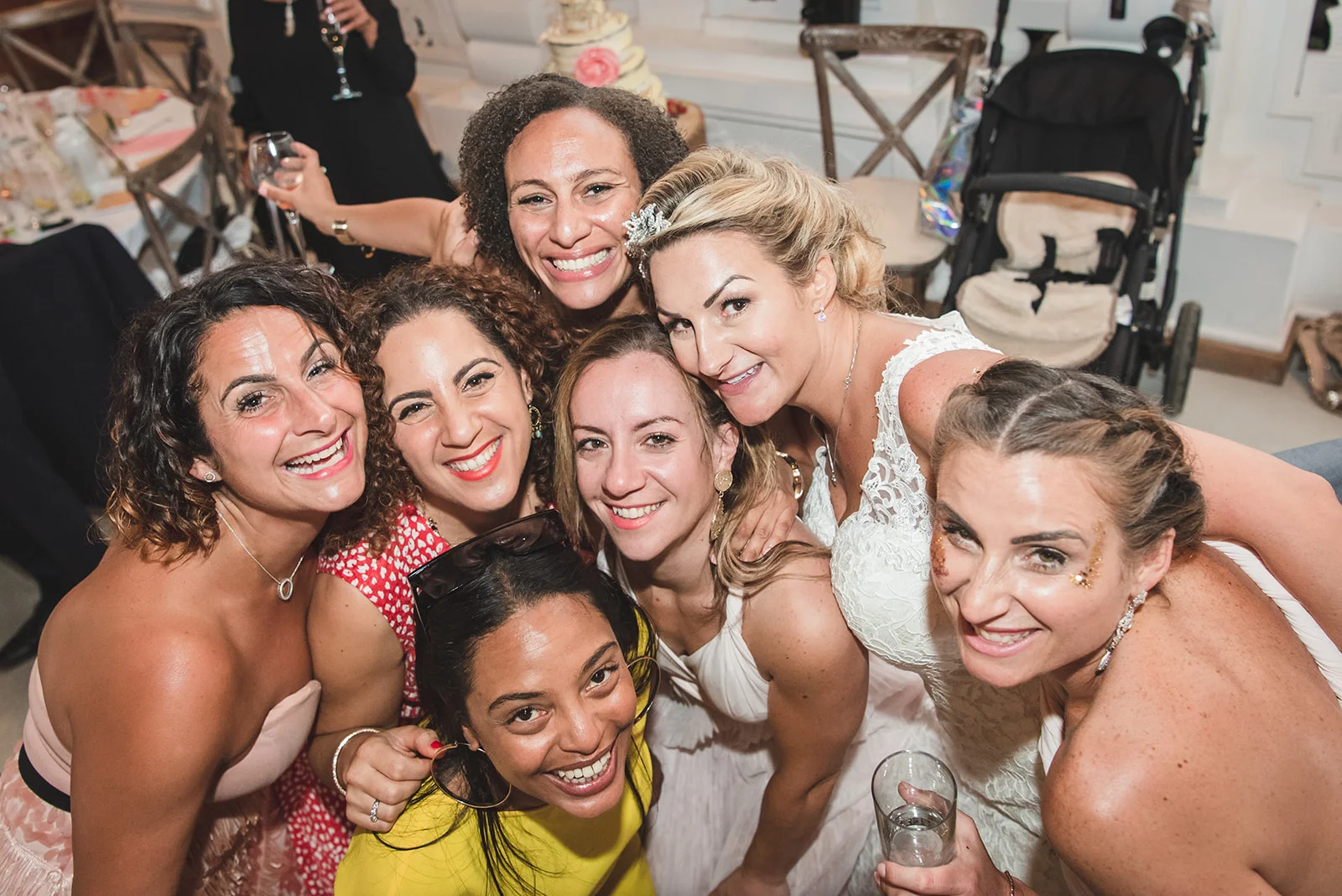 A high angle group shot of smiling wedding guests and the bride leaning in closely together during the evening reception.