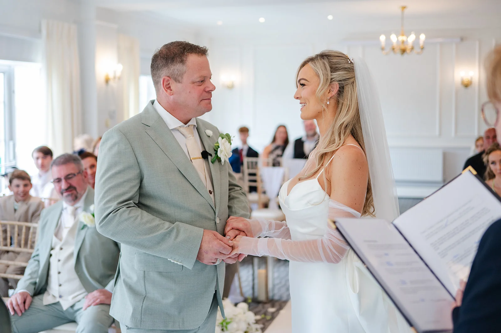 A smiling bride and groom hold hands and exchange vows during their indoor civil ceremony in a bright, modern venue.