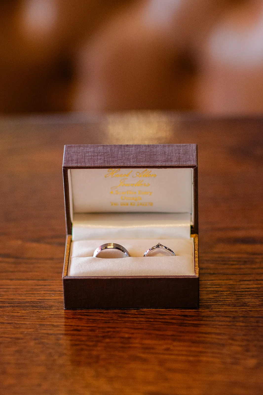 A close up macro shot of two wedding bands resting side by side inside an open presentation box on a dark wooden surface.
