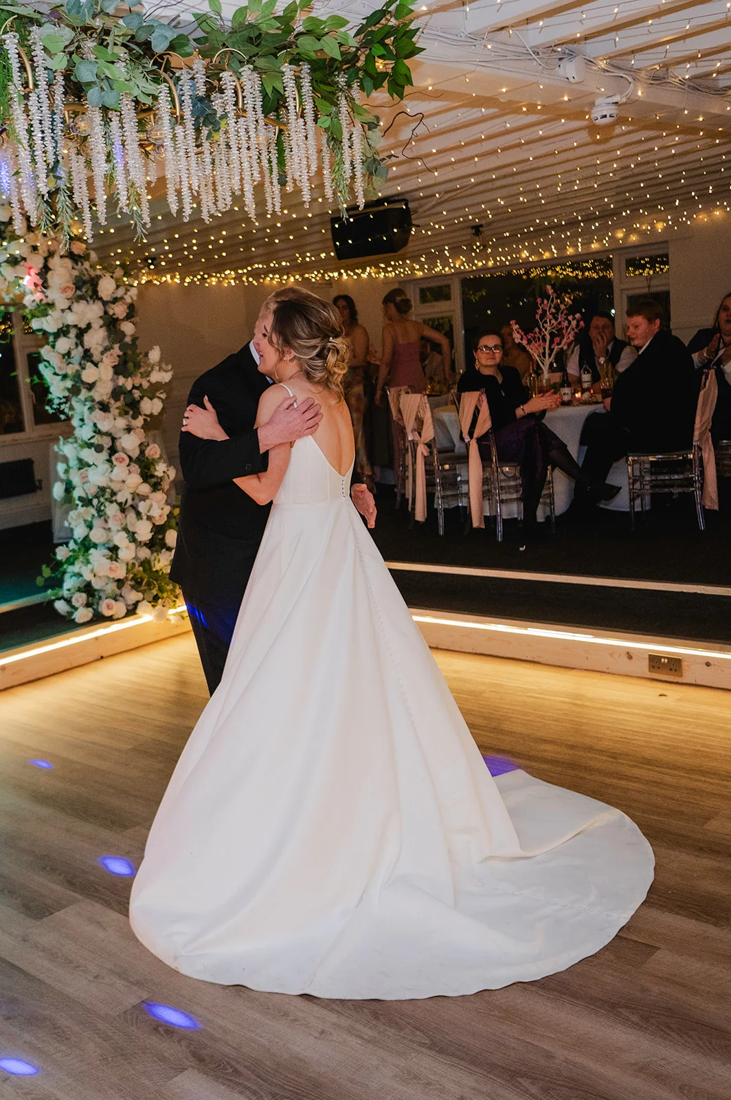 Newlyweds share an intimate first dance under a sparkling fairy light canopy and a magnificent floral hanging installation.