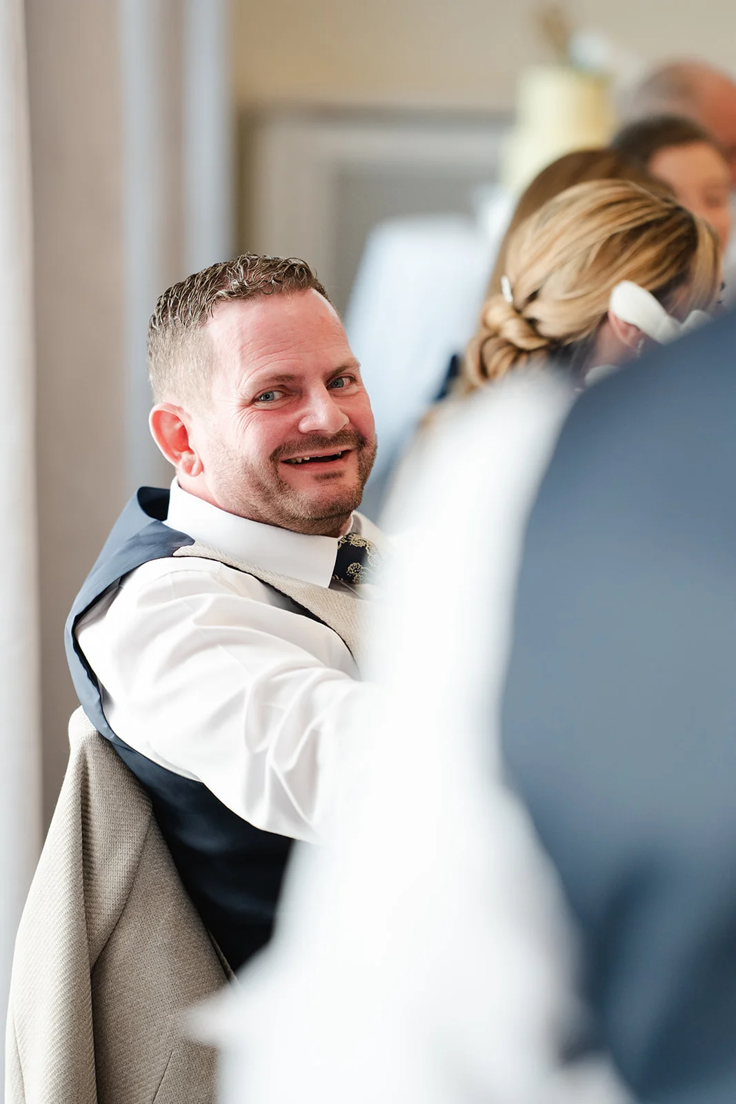 A smiling wedding guest looks back over his shoulder while seated at a table during the wedding reception.