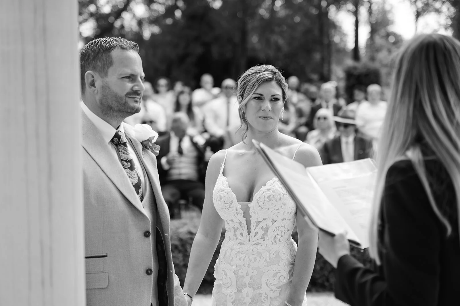 An emotional black and white shot of a bride and groom during an outdoor celebrant-led ceremony, standing together while holding hands.