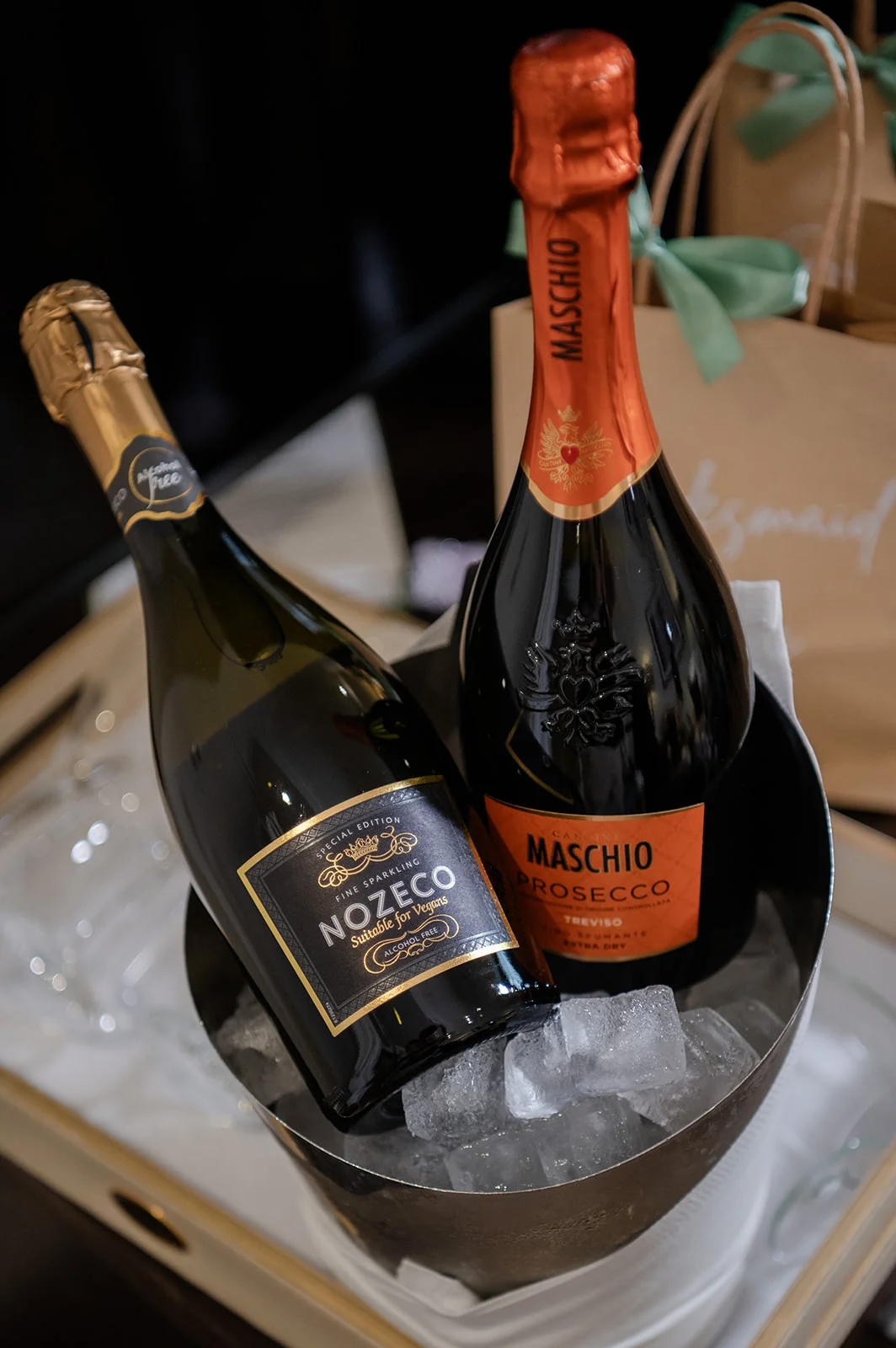 Two chilled bottles of prosecco and sparkling wine rest in an ice bucket, surrounded by elegant glassware and wedding preparations.
