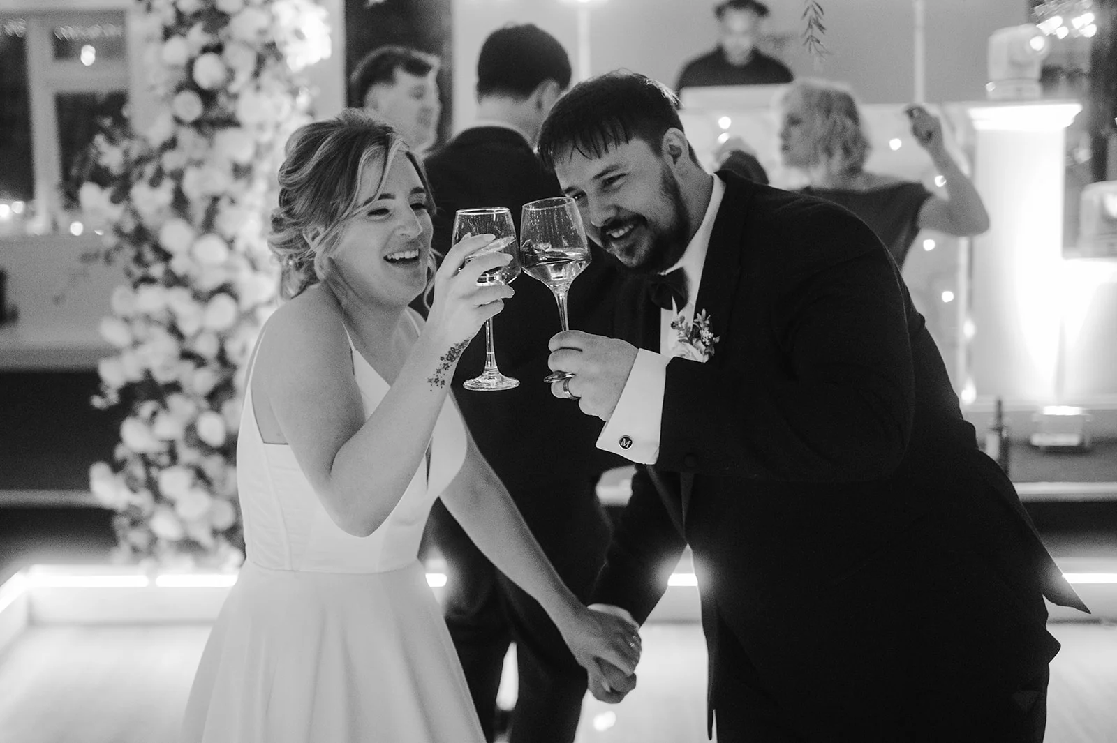 A joyful bride and groom laugh and clink their wine glasses together on the dance floor during their wedding reception.
