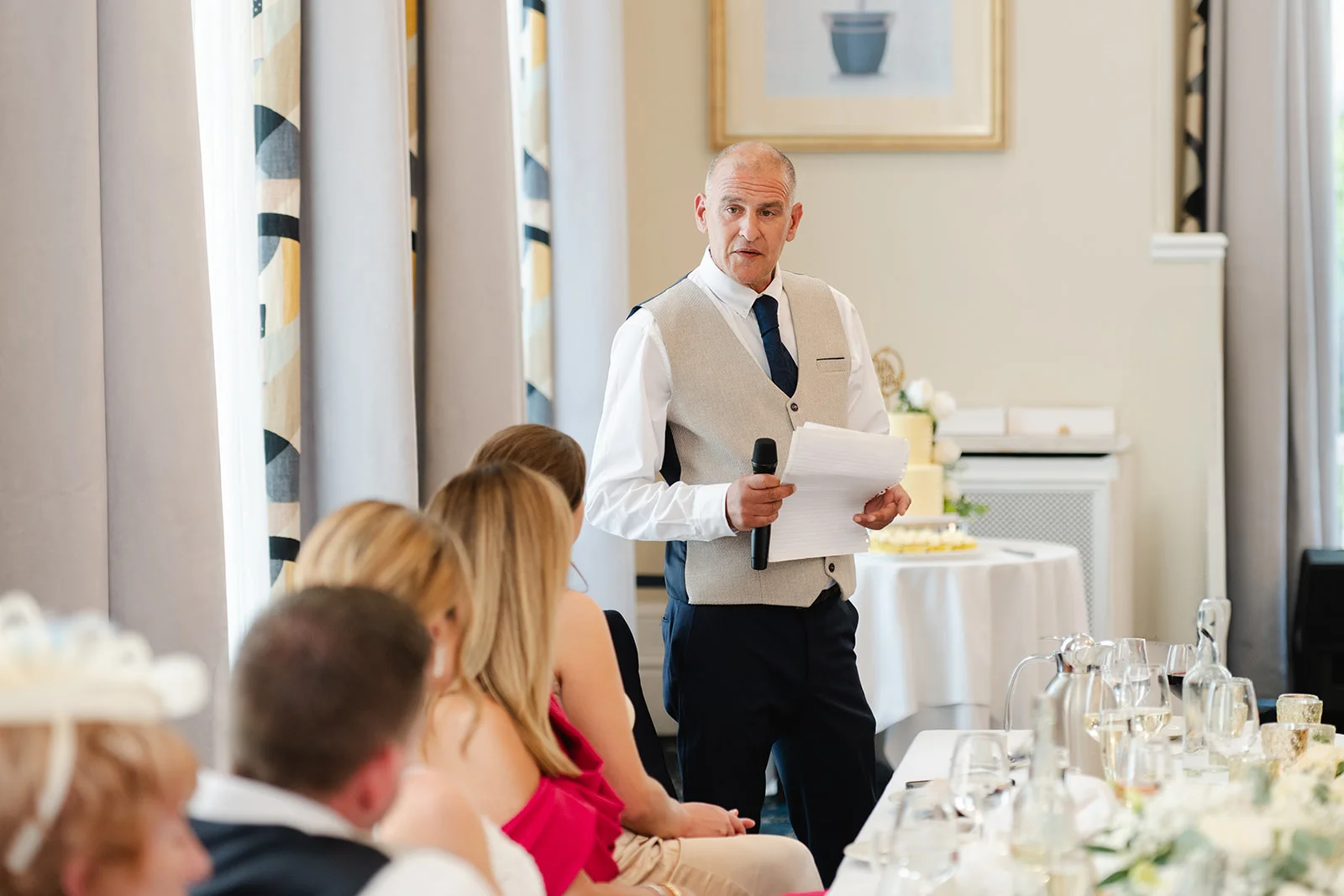 A father of the bride holding a microphone and speech notes delivers a heartfelt speech during the wedding reception.