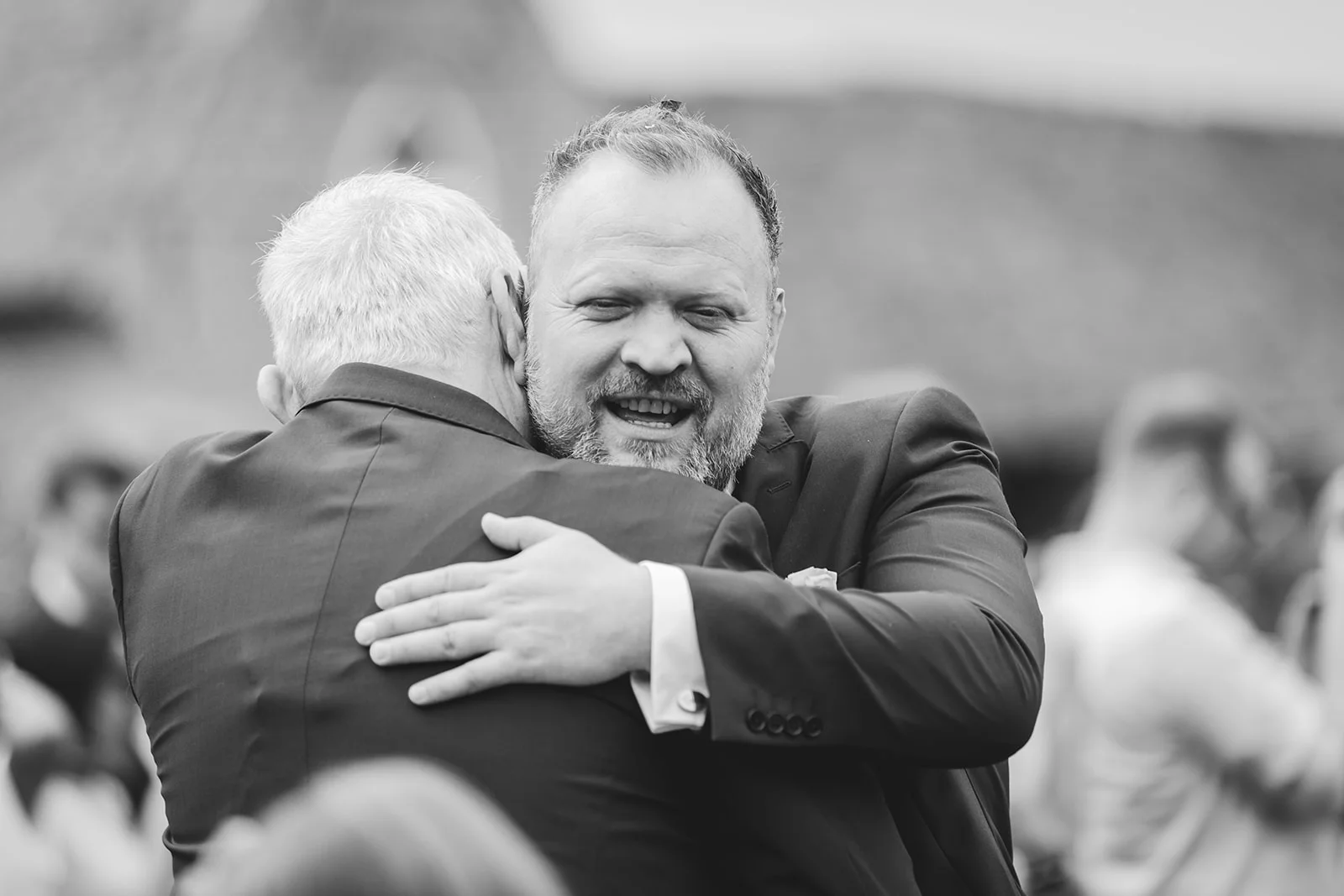 A joyous groom shares a warm, emotional embrace and a heartfelt laugh with a guest during the wedding celebrations.
