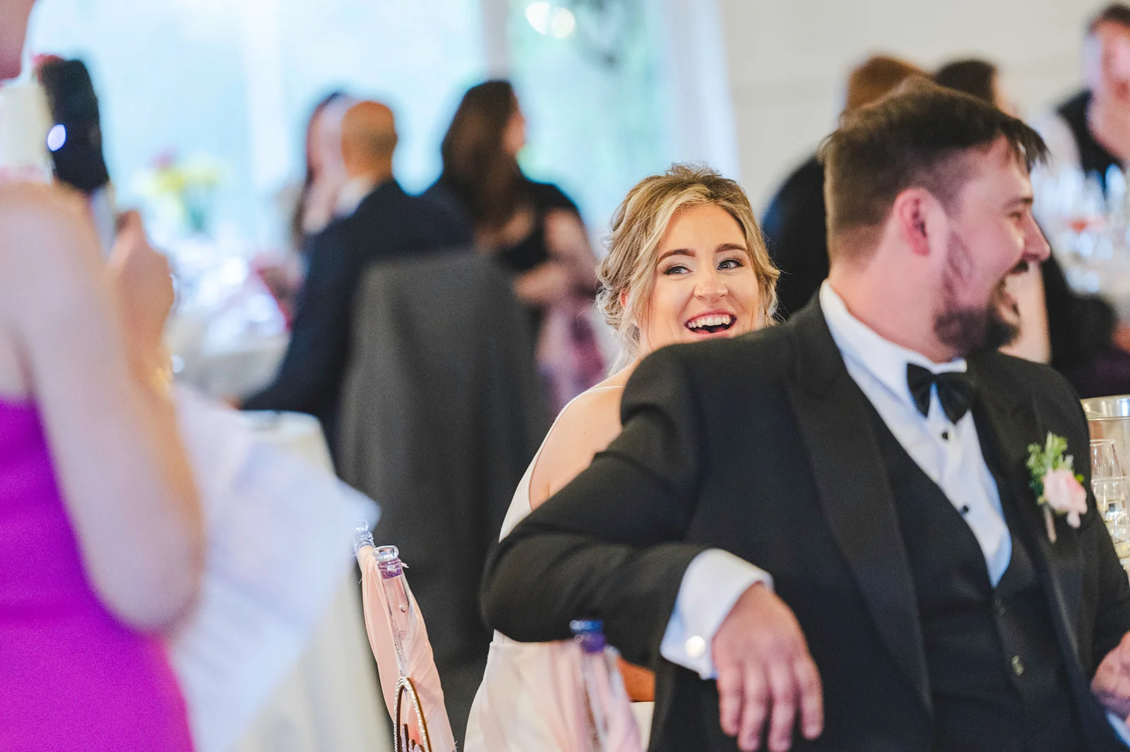 A smiling bride and laughing groom enjoy the wedding speeches at their reception dinner.