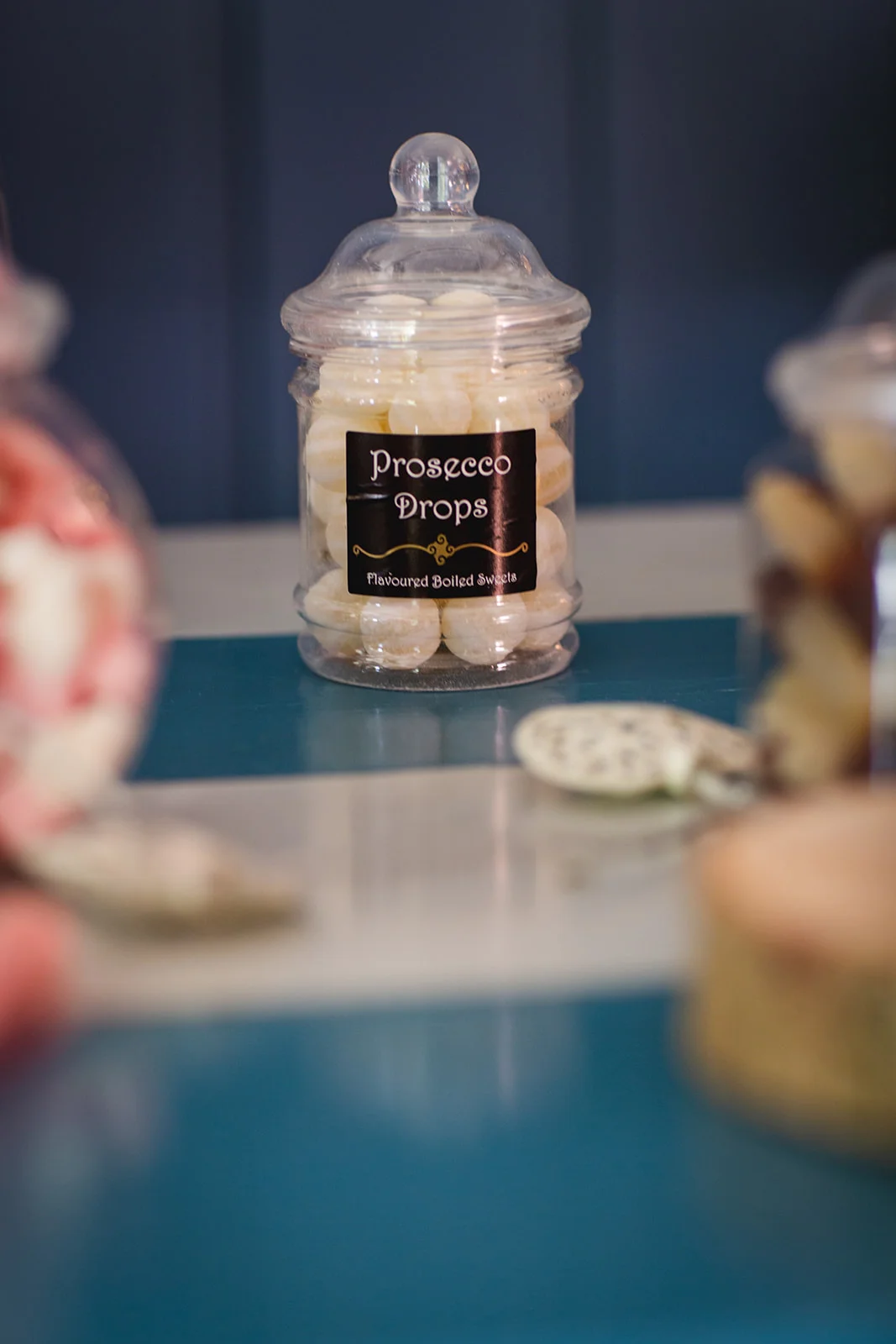 A clear glass jar filled with prosecco drops sweets sits prominently on a table as part of a wedding sweet cart setup.