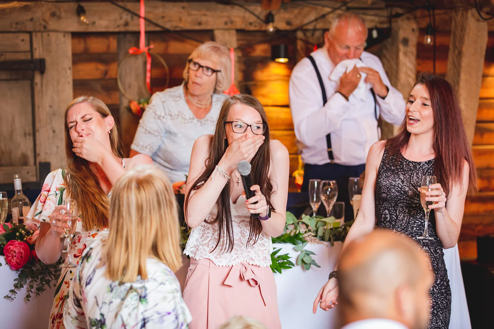 Emotional guests and speakers react with tears and laughter during the wedding speeches inside a rustic wooden barn.