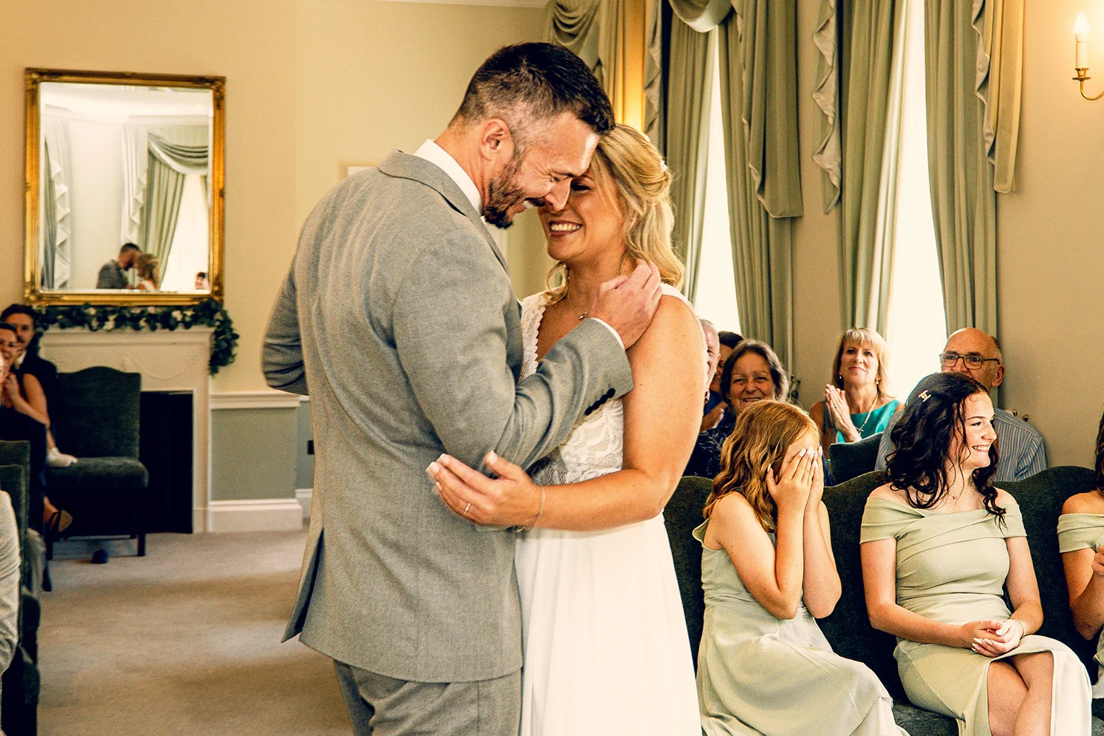 A newlywed couple share a joyful nose-to-nose laugh during their ceremony while guests smile and watch from seated rows.