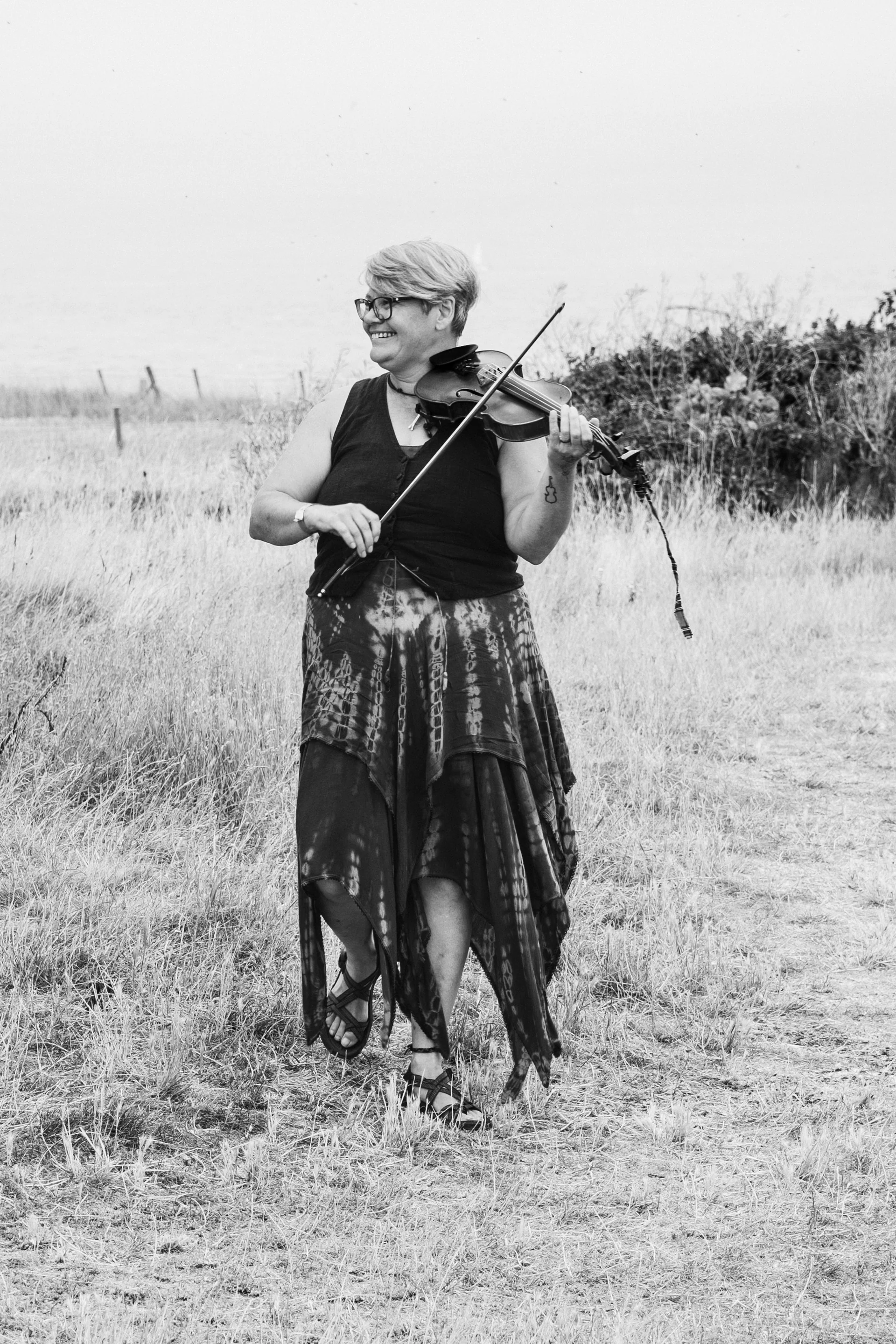 A smiling musician playing the violin while walking through an outdoor meadow during a wedding celebration.