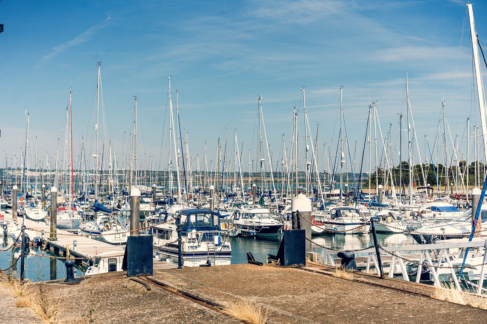 A sunlit marina filled with numerous docked boats and yachts against a clear blue sky.