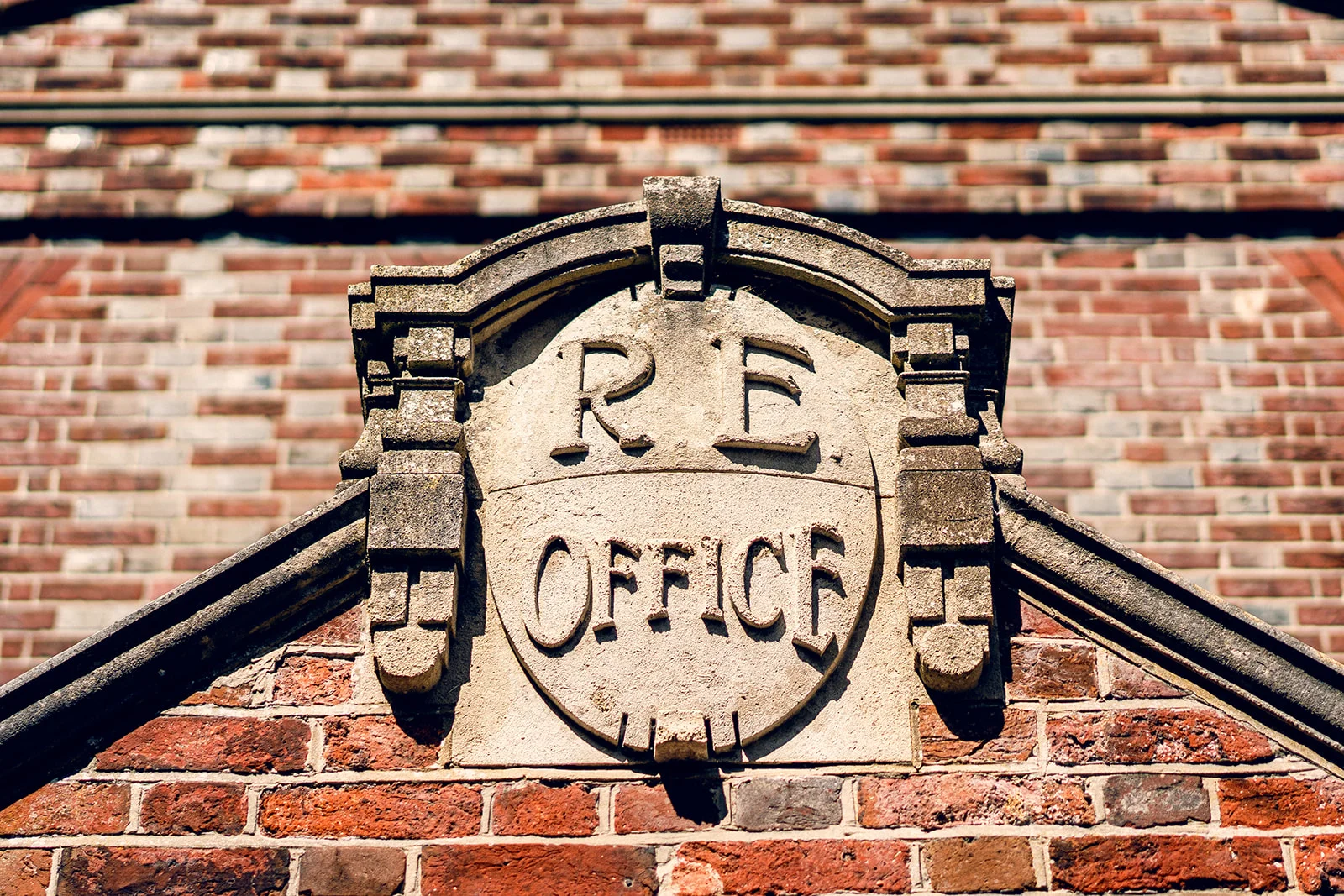 An architectural close-up shot of a carved stone plaque reading R.E. Office mounted on a red brick building exterior.