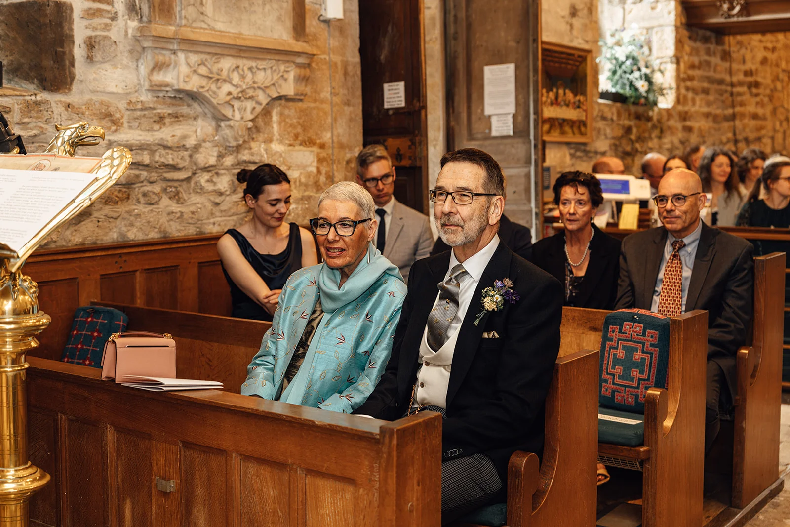 Family members and wedding guests seated in wooden pews inside a historic stone church during the wedding ceremony.