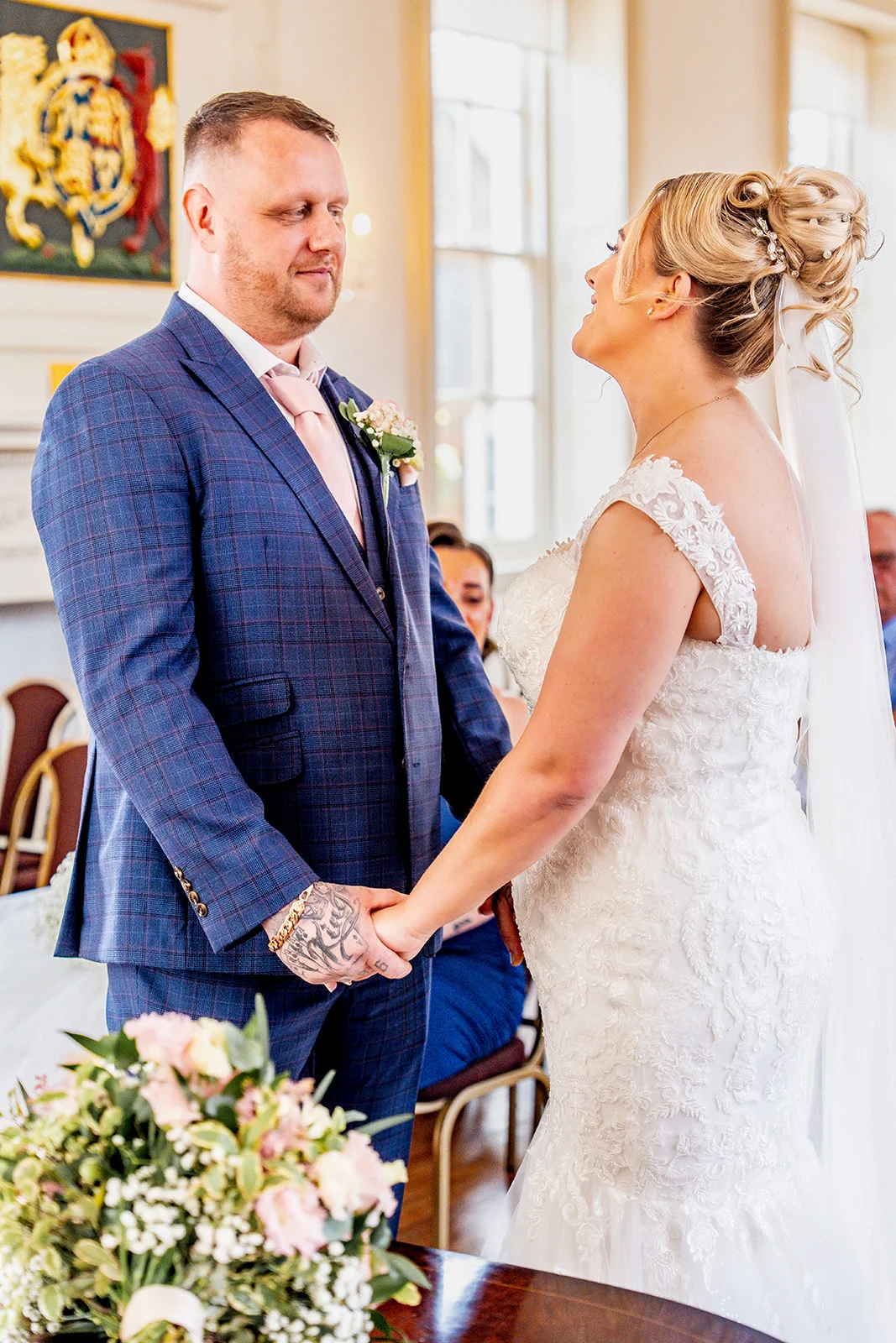 A newlywed couple holding hands and looking lovingly at each other during their registry office wedding ceremony.