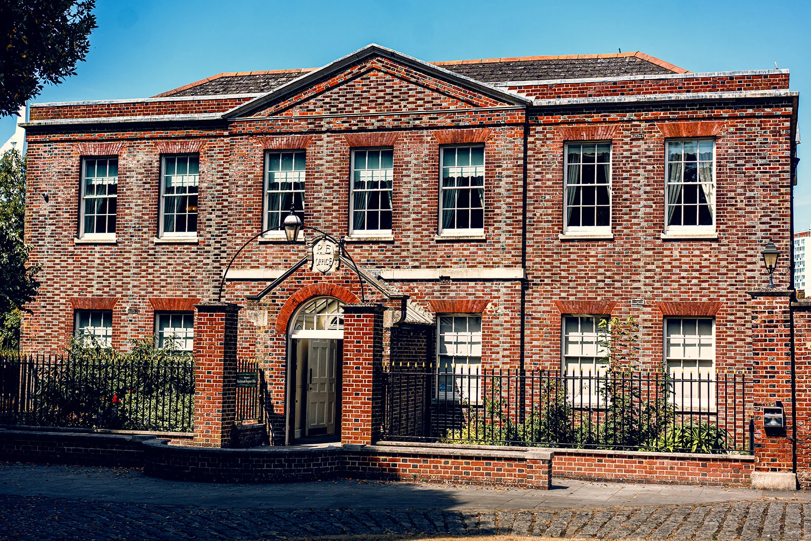 A handsome red brick registry office building featuring traditional multi-pane sash windows, a classical stone archway entrance, and a cobbled courtyard in bright sunlight.
