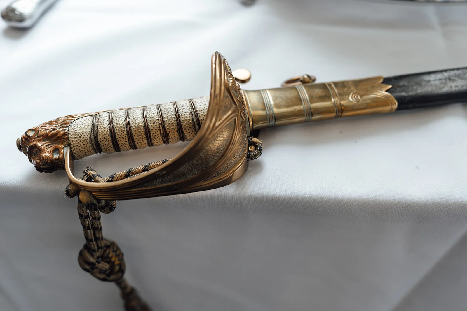 A close-up detail shot shows the ornate golden hilt and lion-head pommel of a military ceremonial sword resting on a white tablecloth.