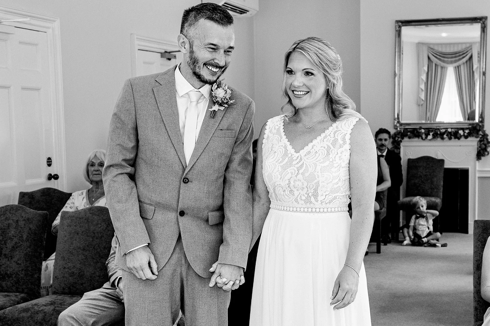 A happy bride and groom holding hands and smiling during their wedding ceremony inside a light room.