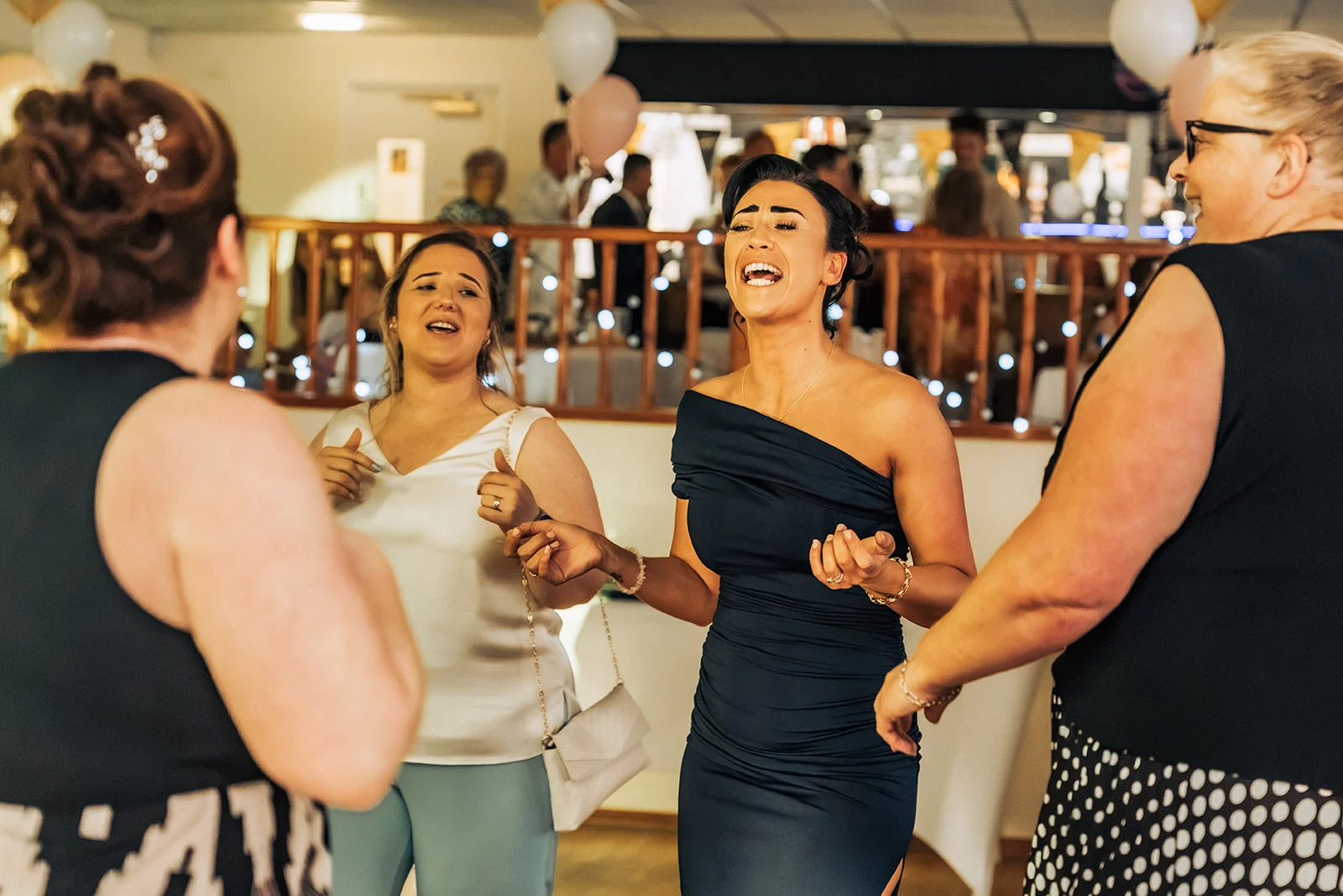 A group of wedding guests dance and laugh joyfully together during the evening reception.