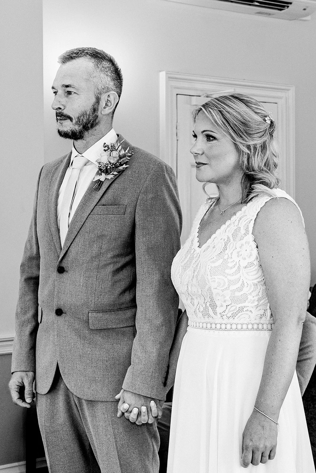 A newlywed couple stands together hand in hand during their civil ceremony, captured in a classic black and white portrait.