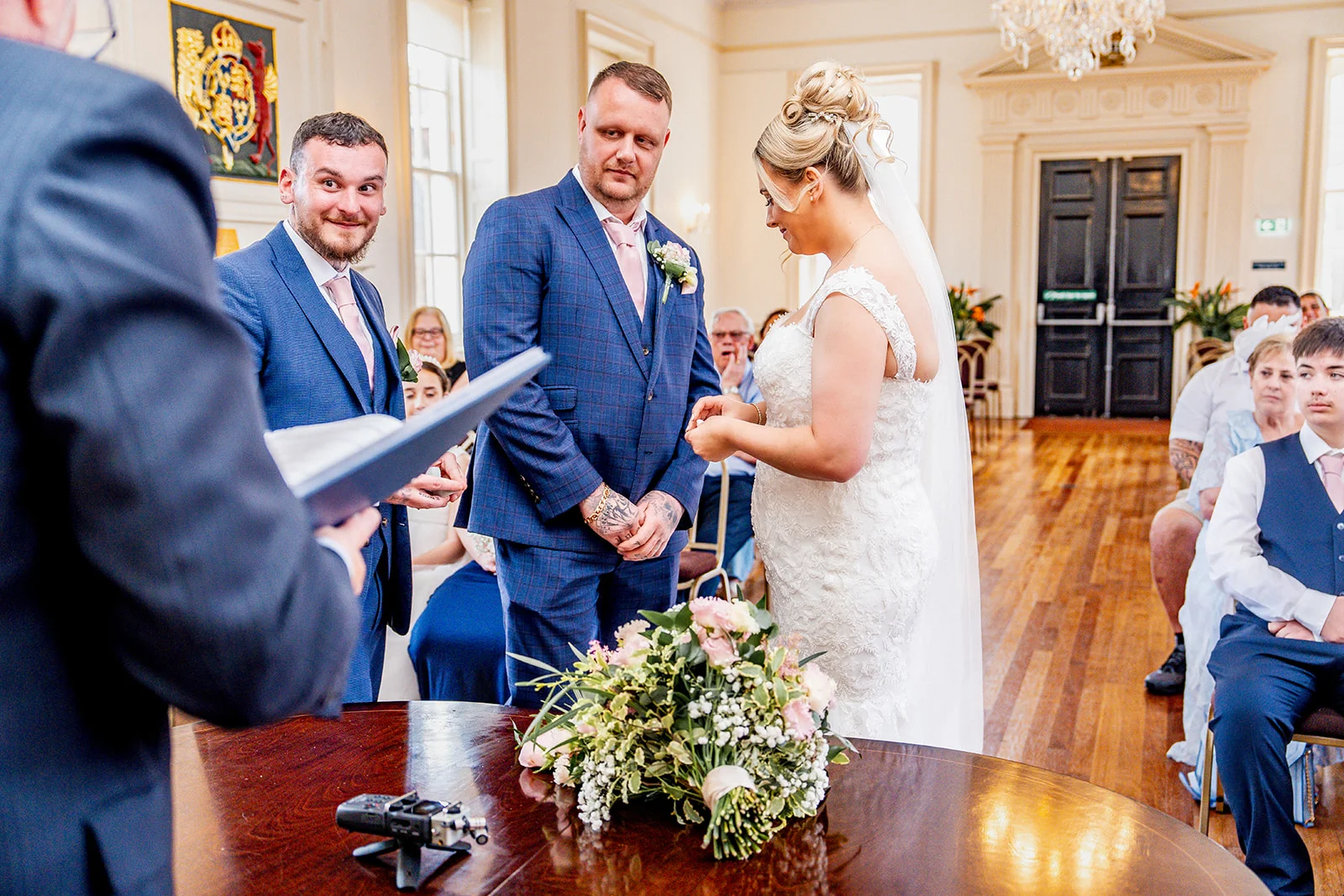 The bride and groom exchange rings during their civil ceremony inside a light-filled registry room while guests look on.