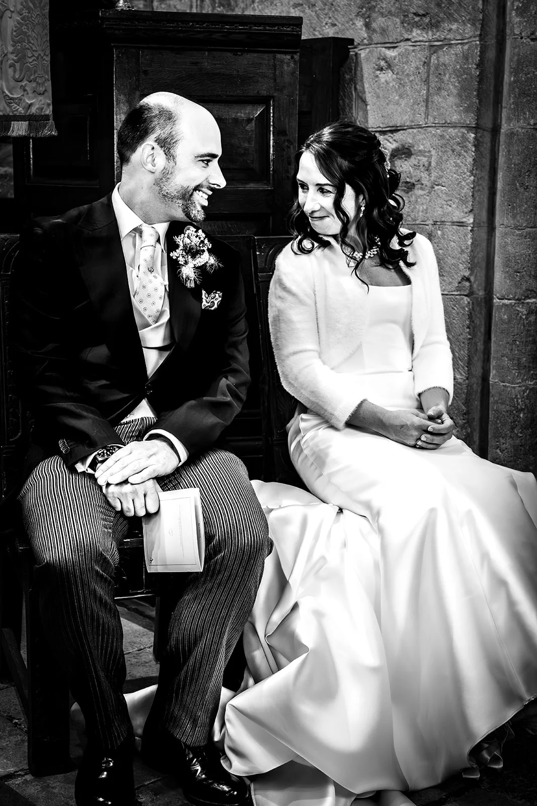 A newlywed couple shares a joyful glance while seated together inside a stone church during their wedding ceremony.