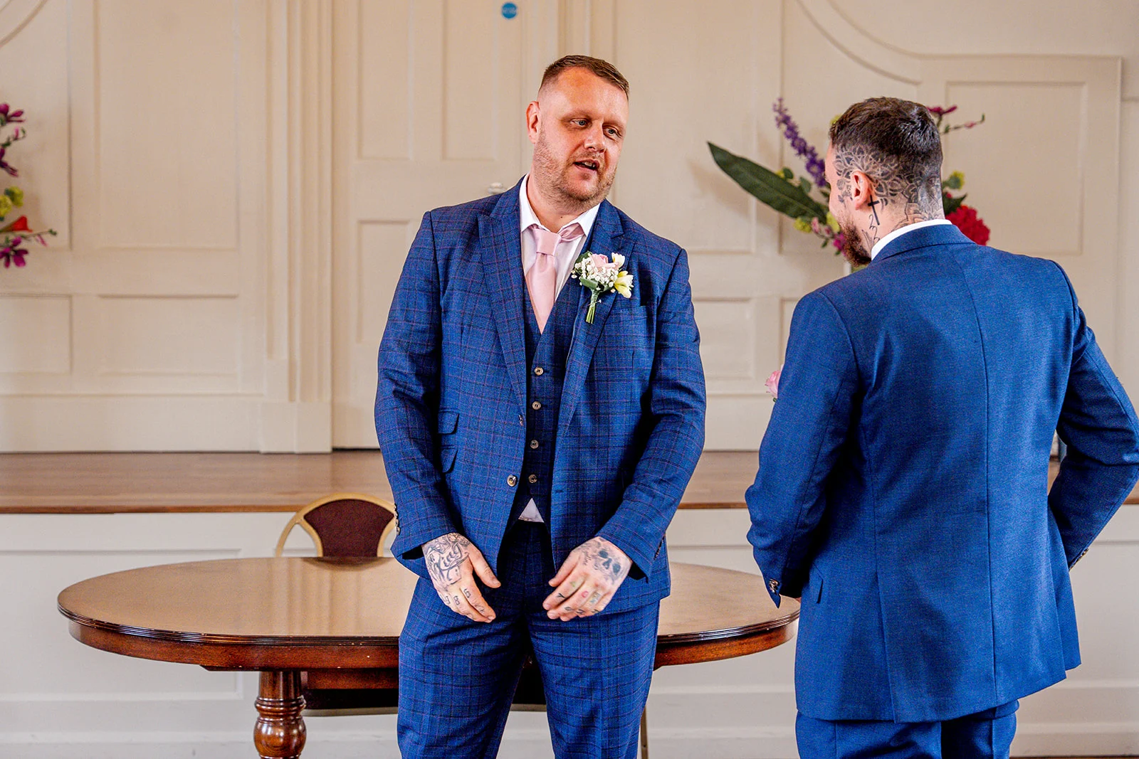 Two grooms in matching blue suits share a moment during their registry office wedding ceremony.