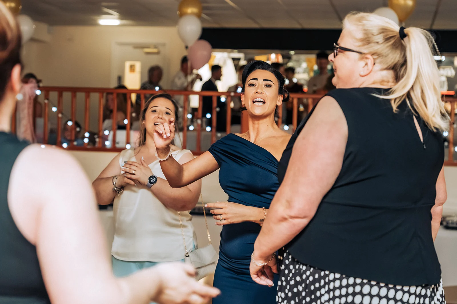 Female wedding guests smiling and dancing together during an evening reception celebration.