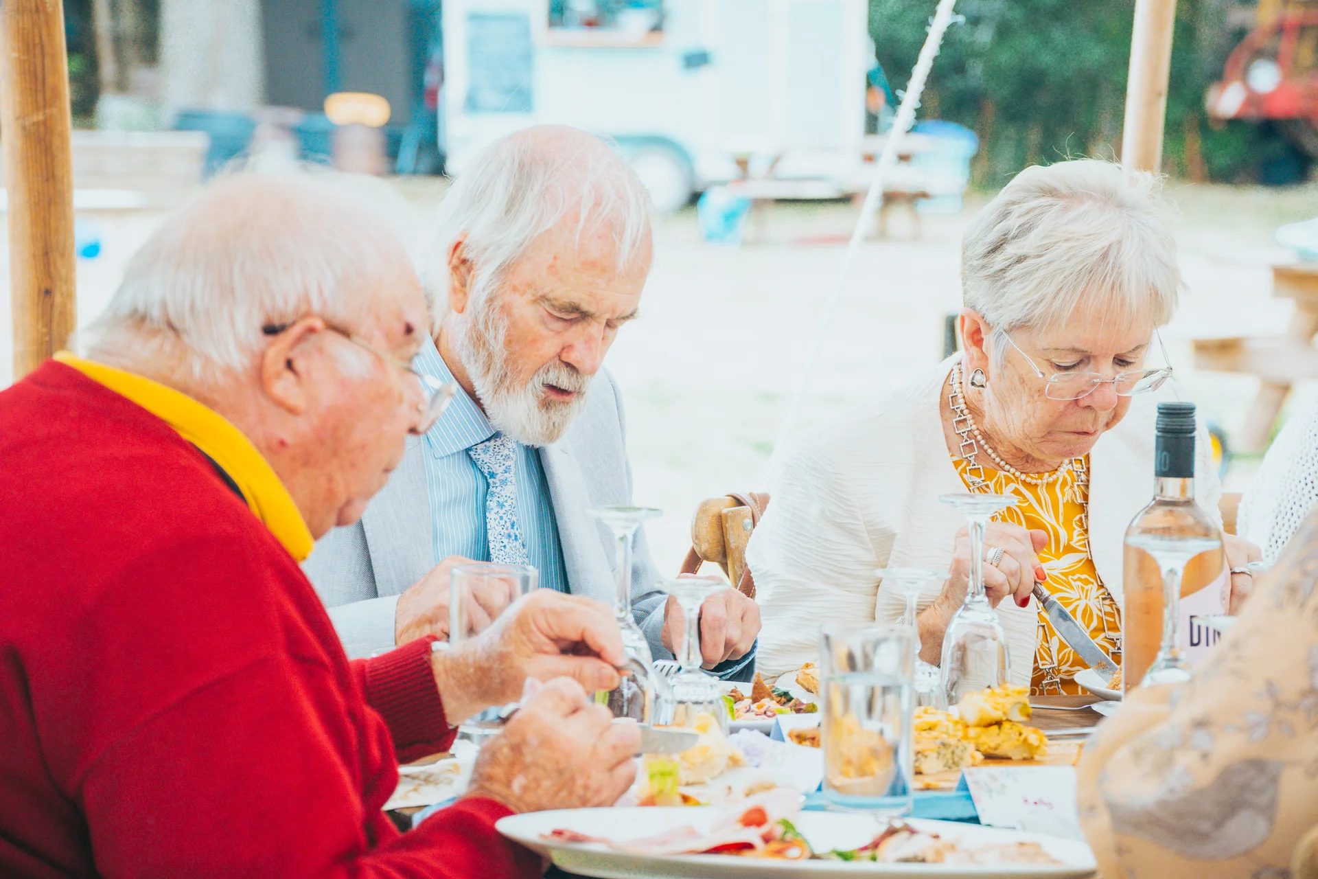 Older wedding guests enjoying a plated meal together at an outdoor reception table.